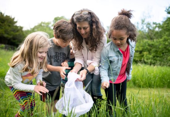 Susie in a meadow with a group of children looking together at an insect net catch.